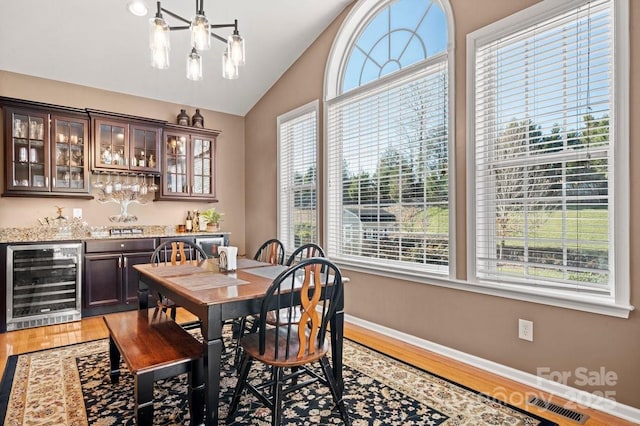 dining room with hardwood / wood-style floors, lofted ceiling, beverage cooler, and bar area