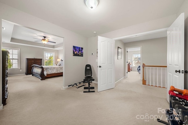 bedroom with a raised ceiling, ceiling fan, and light colored carpet