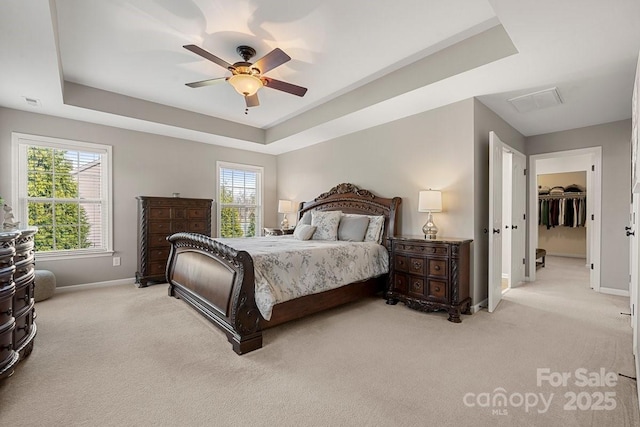 carpeted bedroom with a raised ceiling, multiple windows, ceiling fan, and a closet