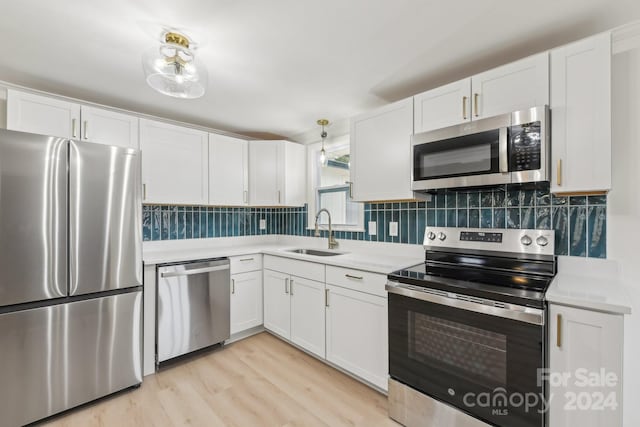 kitchen featuring sink, backsplash, appliances with stainless steel finishes, white cabinets, and light wood-type flooring