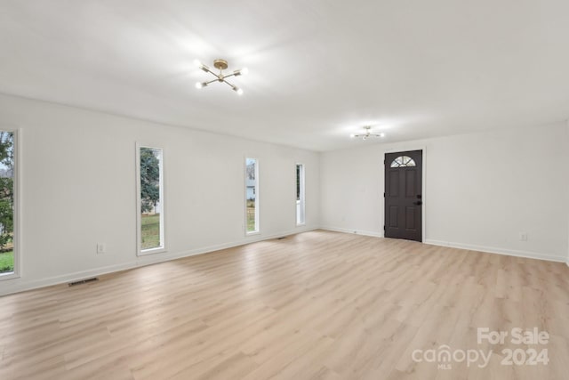 empty room featuring a notable chandelier and light wood-type flooring