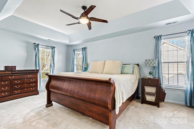 bedroom with a tray ceiling, multiple windows, ceiling fan, and light carpet