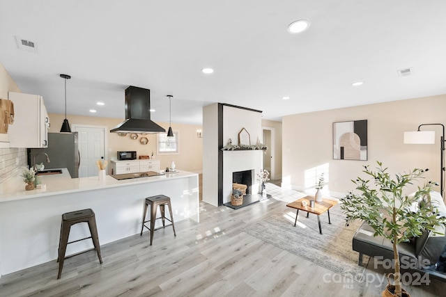 kitchen featuring hanging light fixtures, tasteful backsplash, light hardwood / wood-style floors, kitchen peninsula, and extractor fan