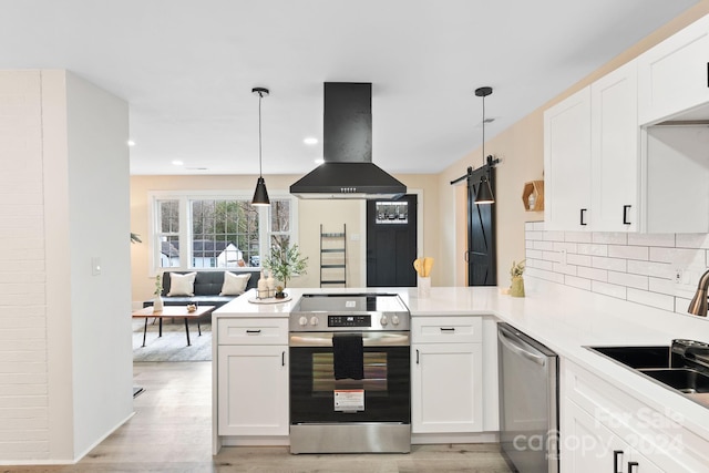 kitchen with a barn door, island range hood, pendant lighting, and appliances with stainless steel finishes