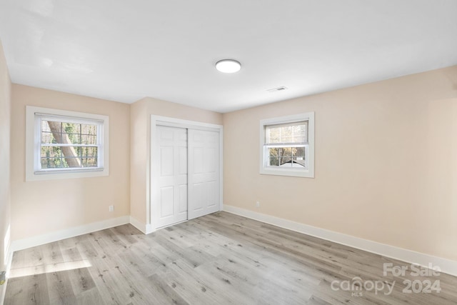 unfurnished bedroom featuring multiple windows, a closet, and light hardwood / wood-style floors