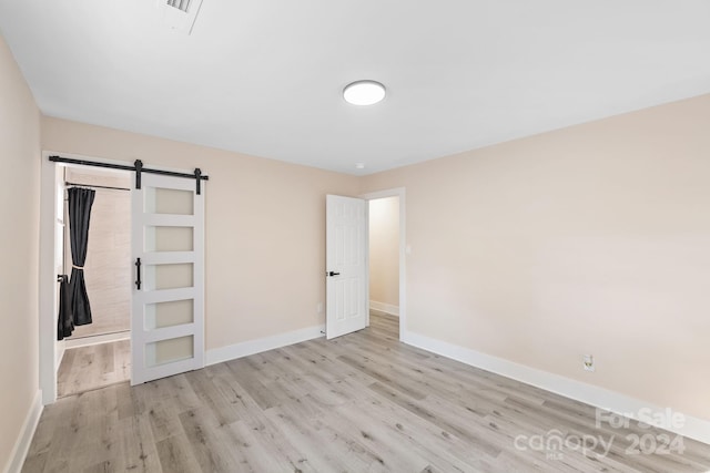 unfurnished bedroom featuring a barn door and light wood-type flooring