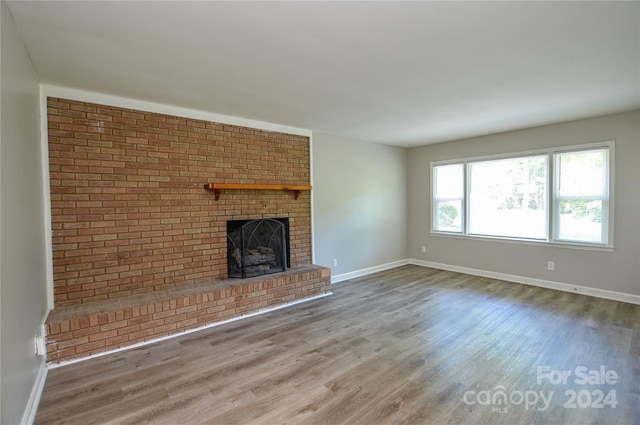 unfurnished living room with wood-type flooring and a brick fireplace