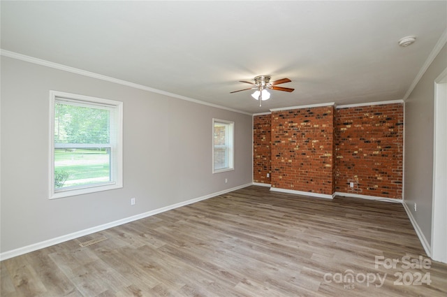 empty room with light wood-type flooring, plenty of natural light, crown molding, and brick wall