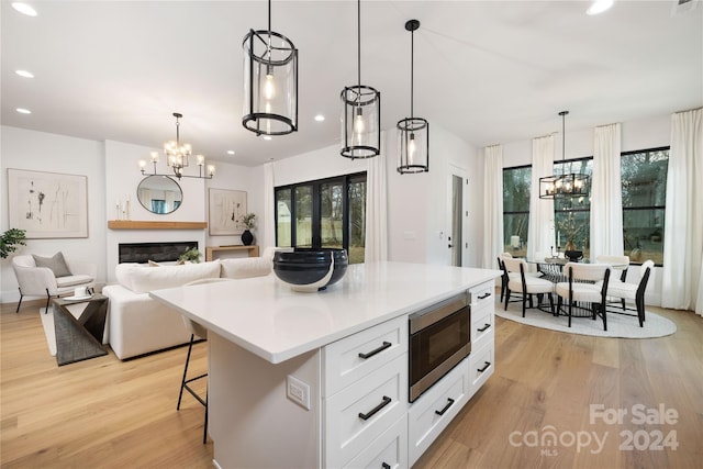 kitchen with stainless steel microwave, hanging light fixtures, a kitchen breakfast bar, white cabinets, and light wood-type flooring