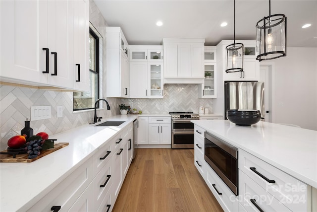 kitchen with white cabinetry, sink, stainless steel appliances, pendant lighting, and light hardwood / wood-style floors