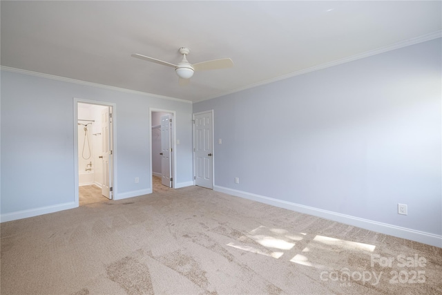 unfurnished bedroom featuring crown molding, ensuite bath, ceiling fan, a walk in closet, and light colored carpet