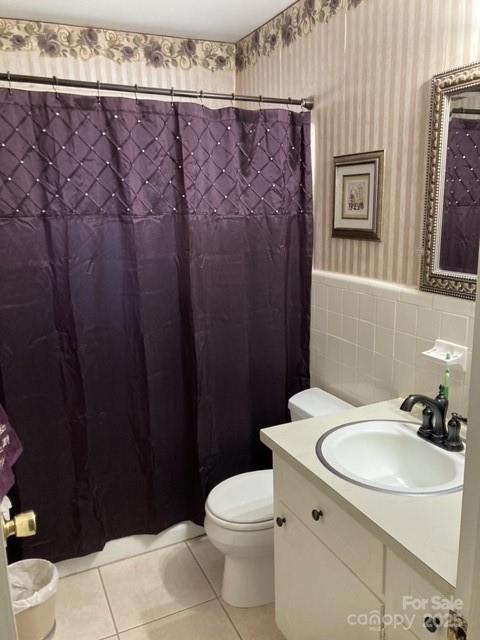 bathroom featuring tile patterned flooring, vanity, tile walls, toilet, and walk in shower