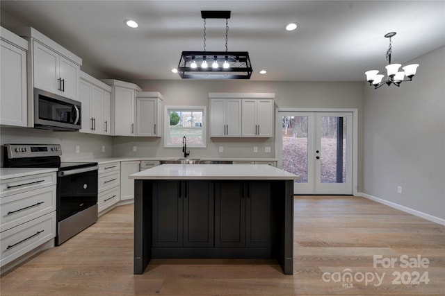 kitchen with a center island, white cabinets, hanging light fixtures, light wood-type flooring, and stainless steel appliances