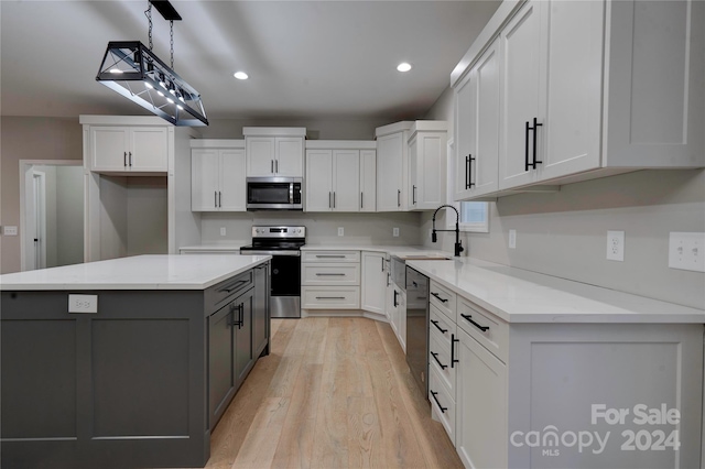 kitchen featuring light wood-type flooring, stainless steel appliances, sink, white cabinets, and a center island