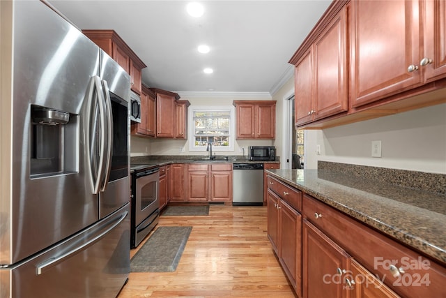 kitchen featuring appliances with stainless steel finishes, crown molding, sink, light hardwood / wood-style flooring, and dark stone countertops