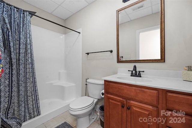 bathroom with a drop ceiling, walk in shower, tile patterned flooring, toilet, and vanity