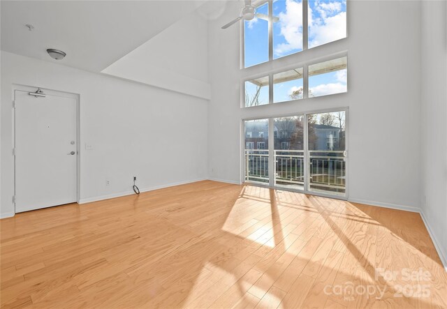 unfurnished living room featuring ceiling fan, light hardwood / wood-style flooring, and a high ceiling