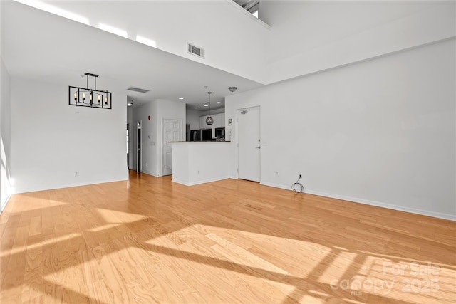 unfurnished living room featuring light hardwood / wood-style floors, a high ceiling, and an inviting chandelier