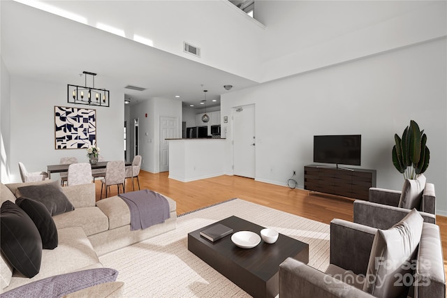 living room with an inviting chandelier, a towering ceiling, and light hardwood / wood-style flooring