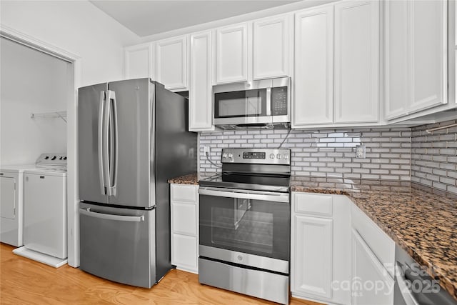 kitchen with white cabinetry, stainless steel appliances, washing machine and dryer, backsplash, and dark stone countertops