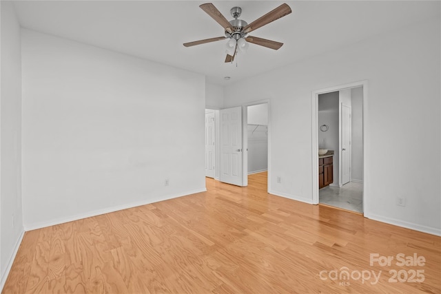 unfurnished bedroom featuring ceiling fan, ensuite bathroom, a walk in closet, a closet, and light wood-type flooring