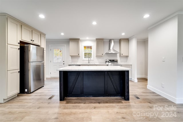 kitchen with wall chimney range hood, sink, ornamental molding, light hardwood / wood-style floors, and stainless steel appliances