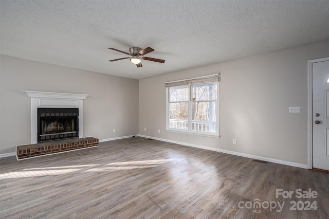 unfurnished living room featuring a textured ceiling, ceiling fan, dark hardwood / wood-style floors, and a brick fireplace