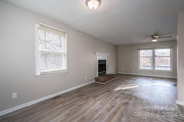 unfurnished living room with hardwood / wood-style floors, a brick fireplace, ceiling fan, and a healthy amount of sunlight