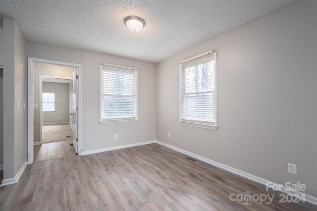 empty room with a textured ceiling and light hardwood / wood-style flooring