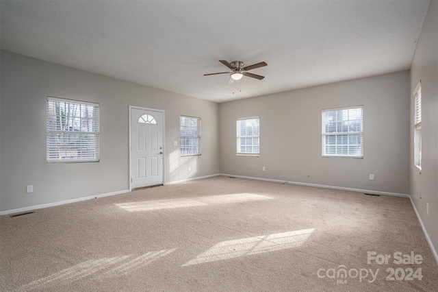 empty room with light carpet, ceiling fan, and a textured ceiling