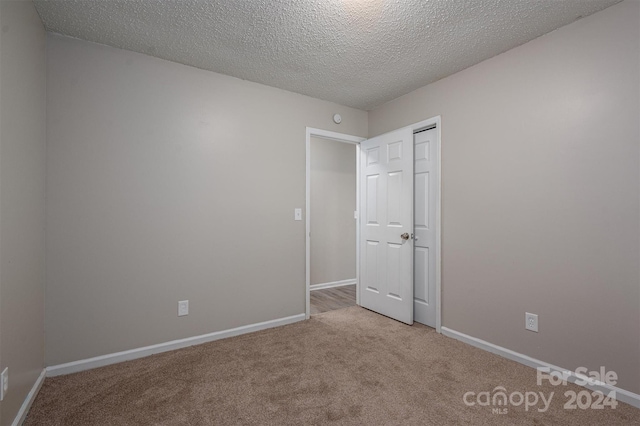 unfurnished bedroom with light carpet, a textured ceiling, and a closet