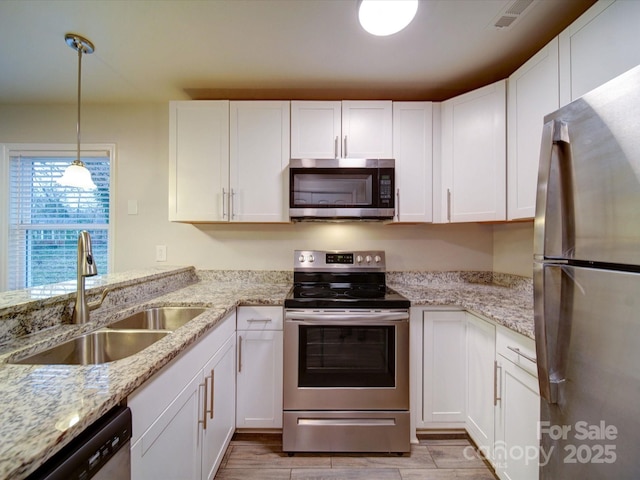 kitchen with appliances with stainless steel finishes, sink, white cabinetry, and pendant lighting