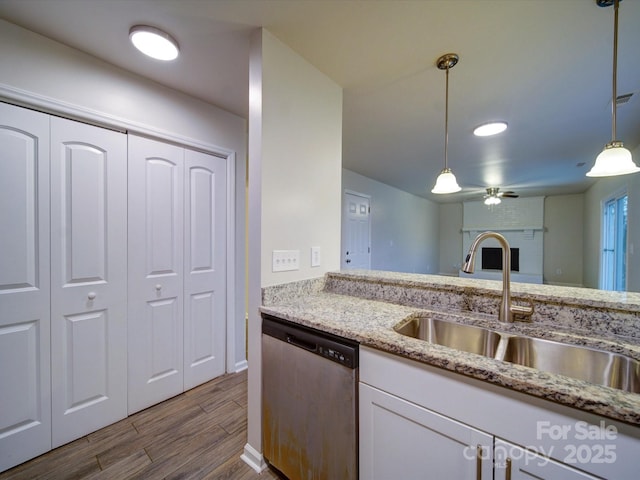 kitchen featuring decorative light fixtures, dishwasher, sink, white cabinetry, and light stone countertops