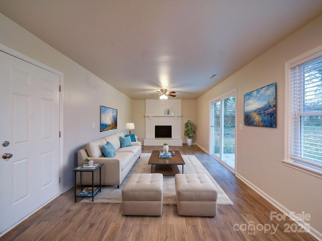 living room featuring ceiling fan, a brick fireplace, wood-type flooring, and a wealth of natural light