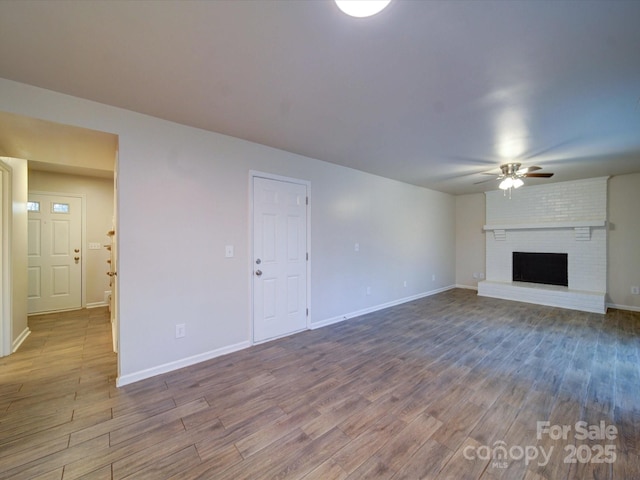 unfurnished living room with a brick fireplace, hardwood / wood-style flooring, and ceiling fan