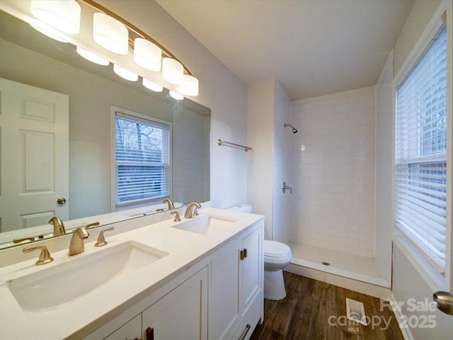 bathroom featuring hardwood / wood-style flooring, toilet, vanity, and a tile shower