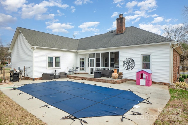 rear view of house with outdoor lounge area, a patio, and a covered pool