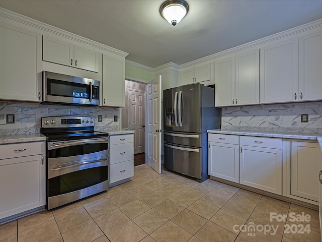 kitchen with appliances with stainless steel finishes, backsplash, light stone counters, light tile patterned floors, and white cabinetry