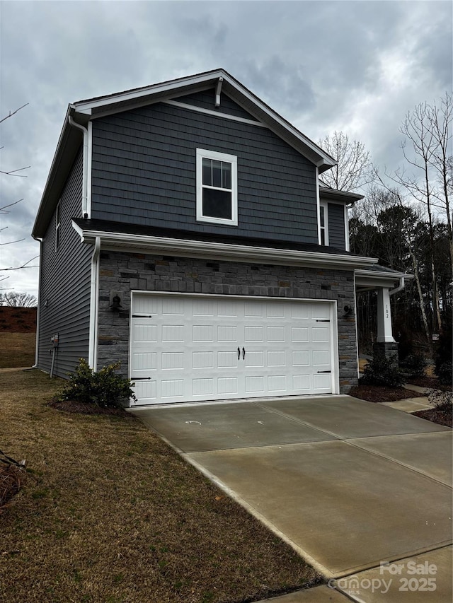 view of side of home with an attached garage, stone siding, concrete driveway, and a yard