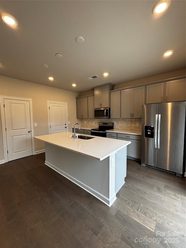 kitchen with a kitchen island with sink, stainless steel appliances, a sink, light countertops, and gray cabinets