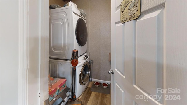 clothes washing area featuring wood-type flooring and stacked washing maching and dryer