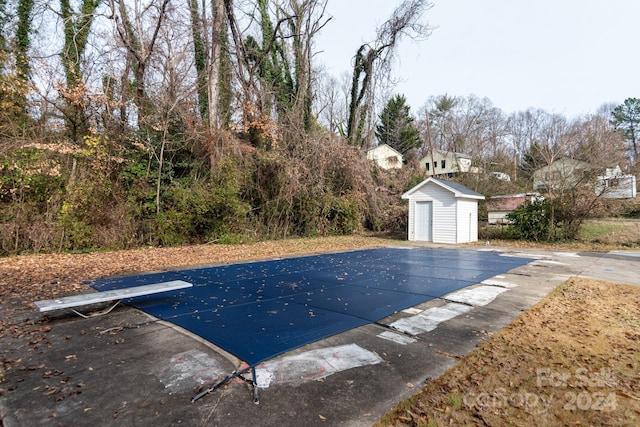 view of pool featuring a diving board, a patio, and a storage shed