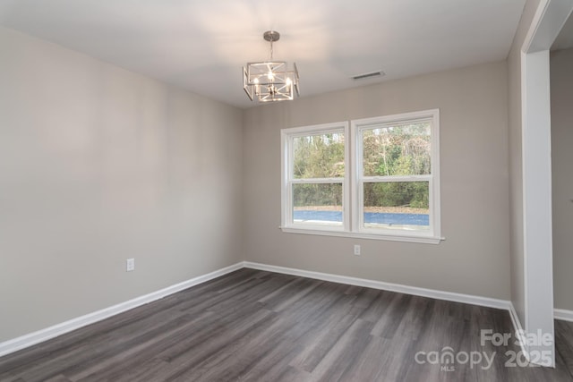 spare room featuring dark wood-type flooring, an inviting chandelier, visible vents, and baseboards