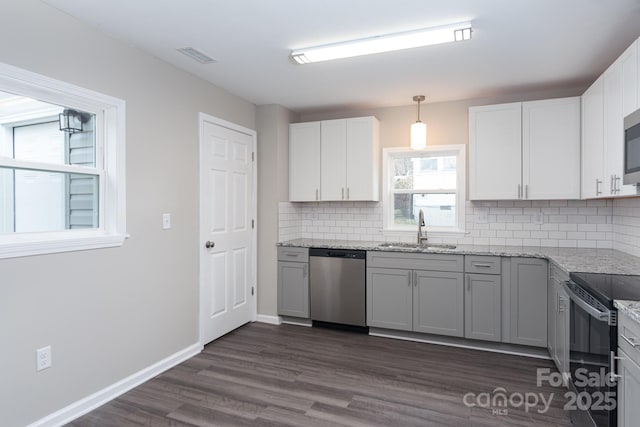 kitchen featuring dark wood finished floors, a sink, light stone countertops, stainless steel appliances, and backsplash