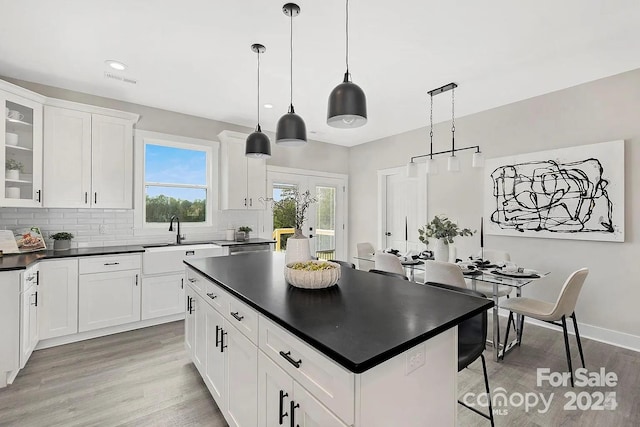 kitchen with decorative light fixtures, dark countertops, glass insert cabinets, white cabinetry, and a sink