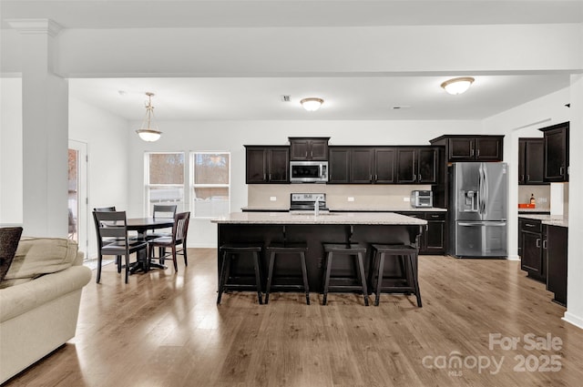 kitchen featuring a breakfast bar, a kitchen island with sink, hanging light fixtures, dark brown cabinets, and stainless steel appliances