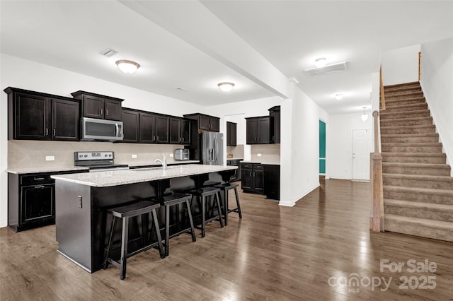 kitchen with appliances with stainless steel finishes, sink, a breakfast bar area, dark hardwood / wood-style flooring, and a kitchen island with sink