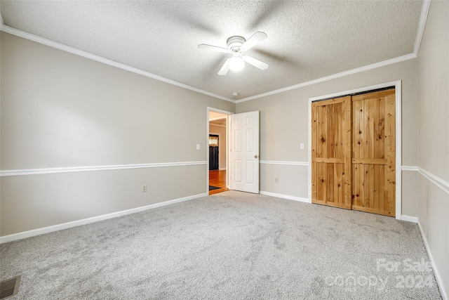 unfurnished bedroom featuring ornamental molding, a textured ceiling, ceiling fan, carpet floors, and a closet