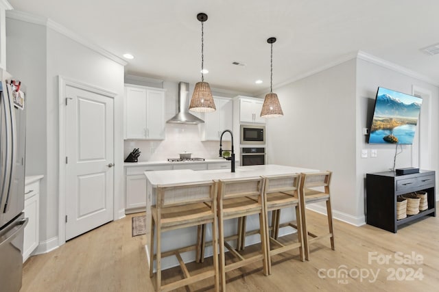 kitchen with white cabinets, appliances with stainless steel finishes, light hardwood / wood-style flooring, and wall chimney range hood