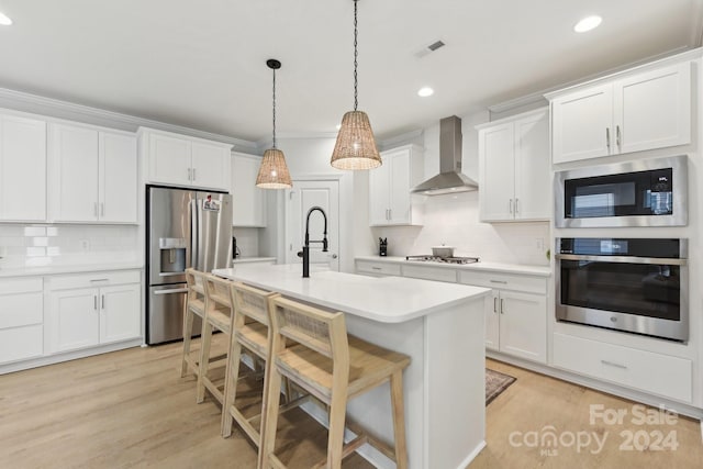 kitchen featuring wall chimney exhaust hood, light hardwood / wood-style floors, decorative light fixtures, white cabinets, and appliances with stainless steel finishes